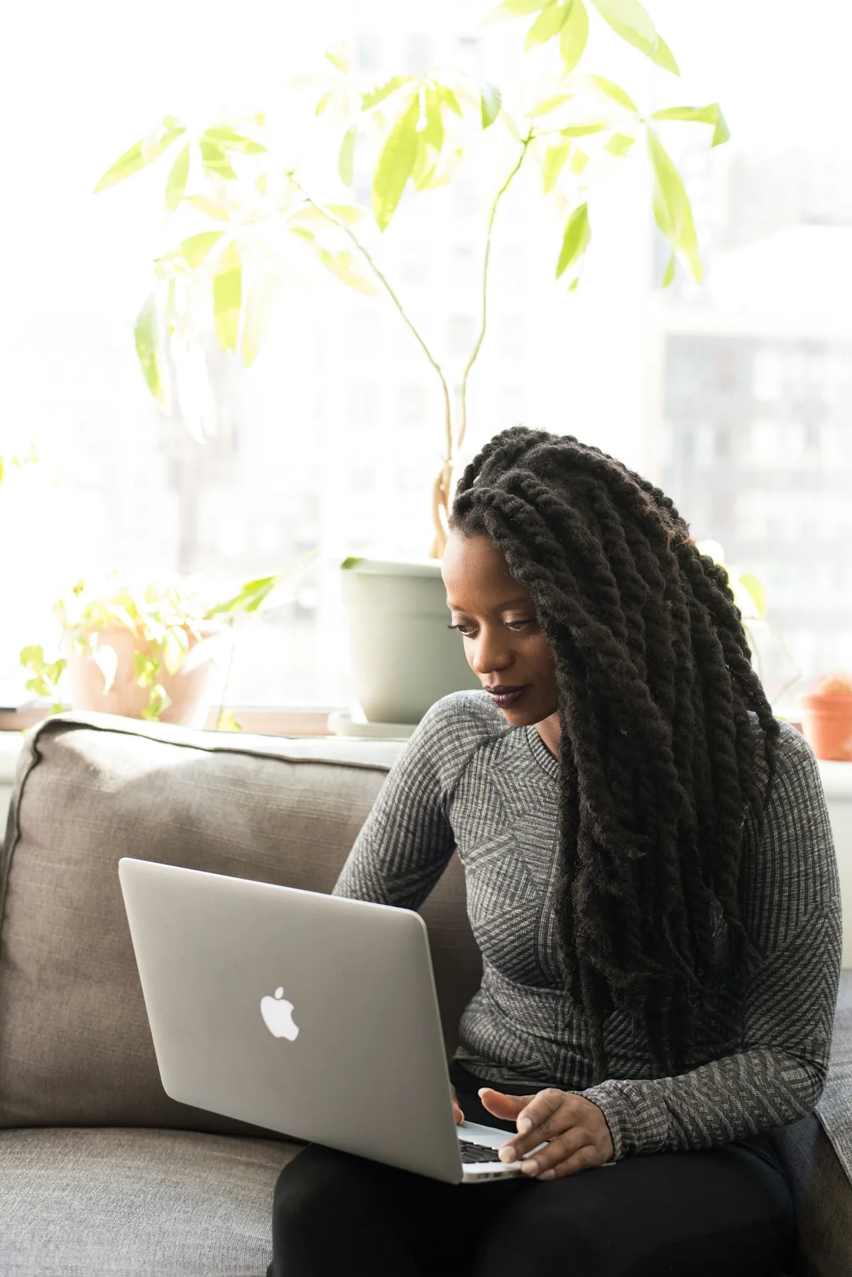 A woman working on her laptop on a sofa by a sunny window